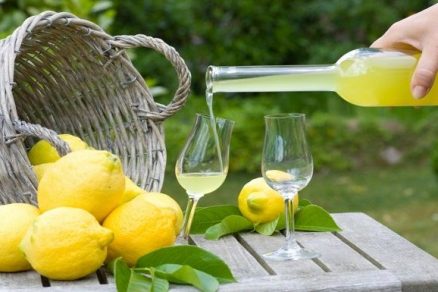 cesta com limões encima de uma mesa no meio de um jardim e uma mão servindo uma taça com limoncello, um dos drinks italianos