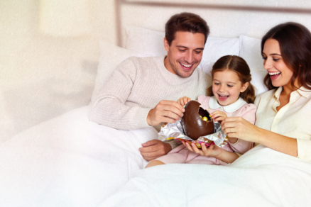 Família alegre na cama abrindo um ovo de páscoa.