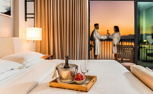 Casal hospedados em uma suíte do Grand Hyatt comemorando dia dos namorados com uma champanheira em cima da cama